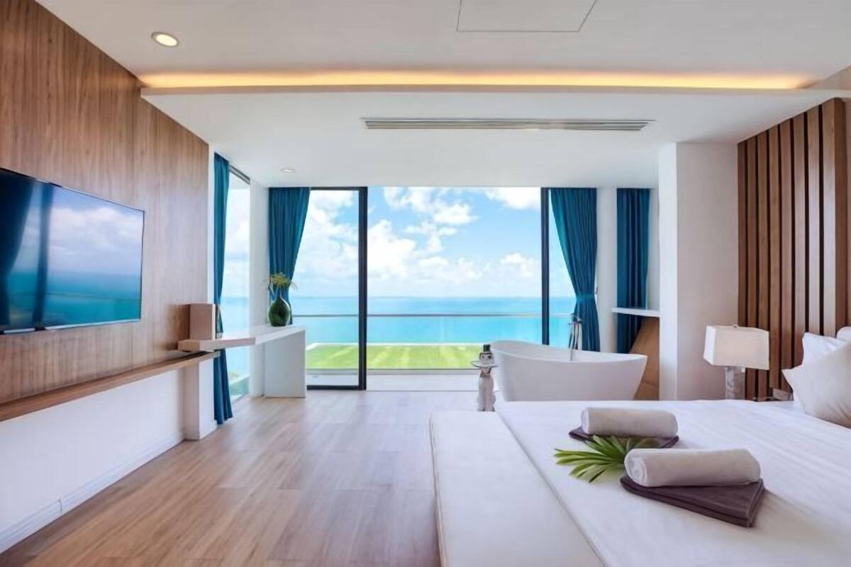 A modern hotel room with a large bed, a TV, a balcony with a view, and a bathroom.