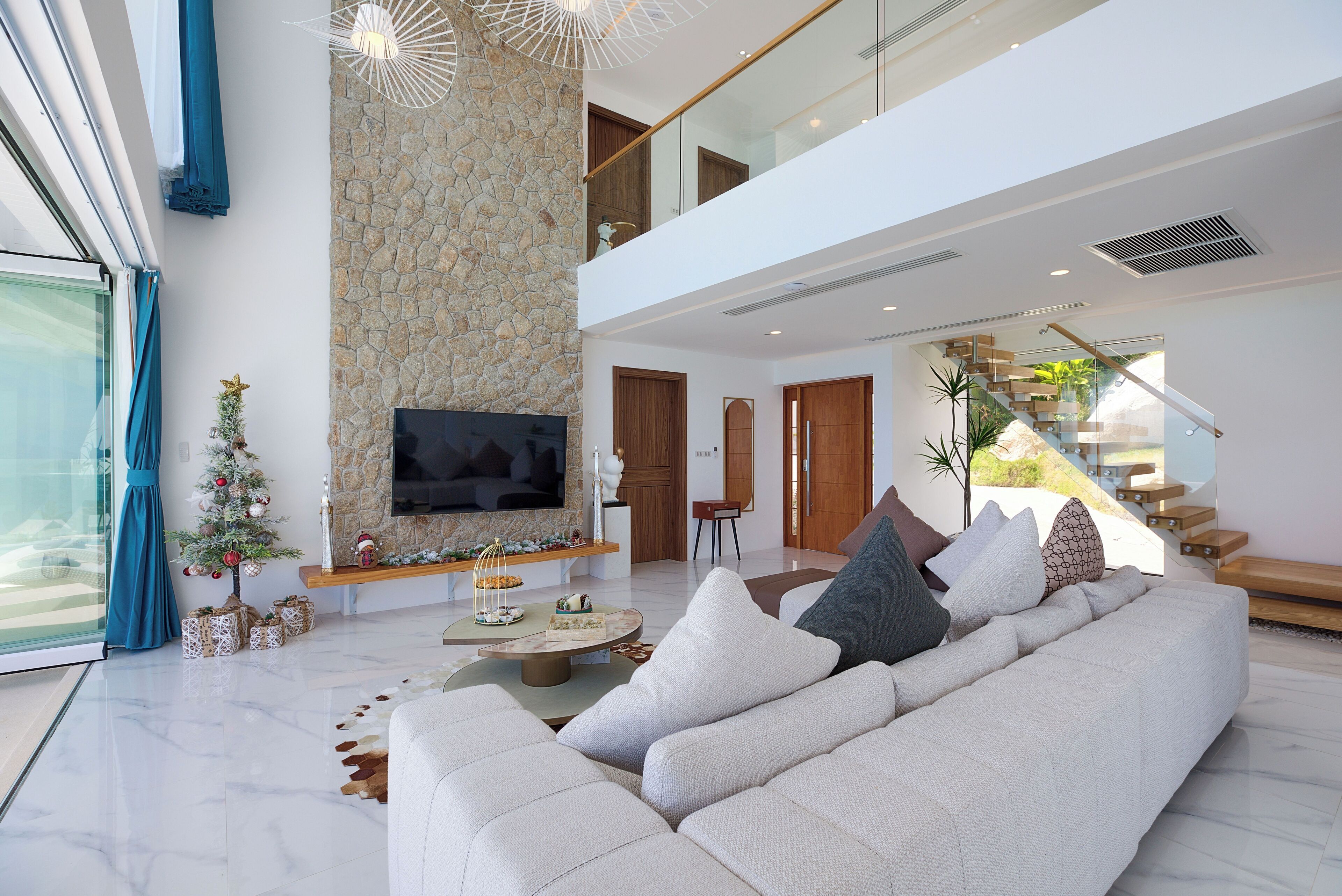 A modern living room with a stone accent wall, a flat-screen TV, a large sofa, and a staircase leading to an upper level.