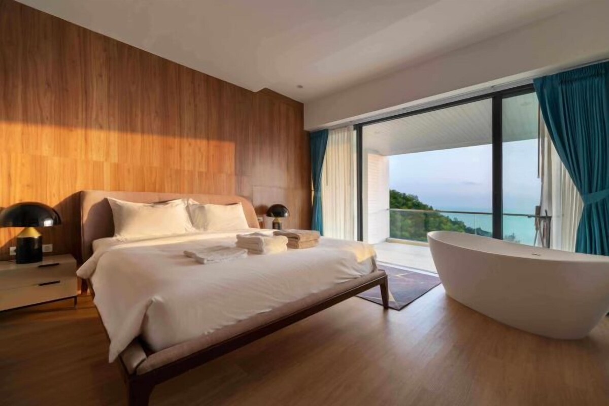 A modern bedroom with a large bed, a bathtub, and a view of the sea.