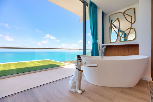 A modern bathroom with a freestanding bathtub, a large mirror, and a view of the ocean.