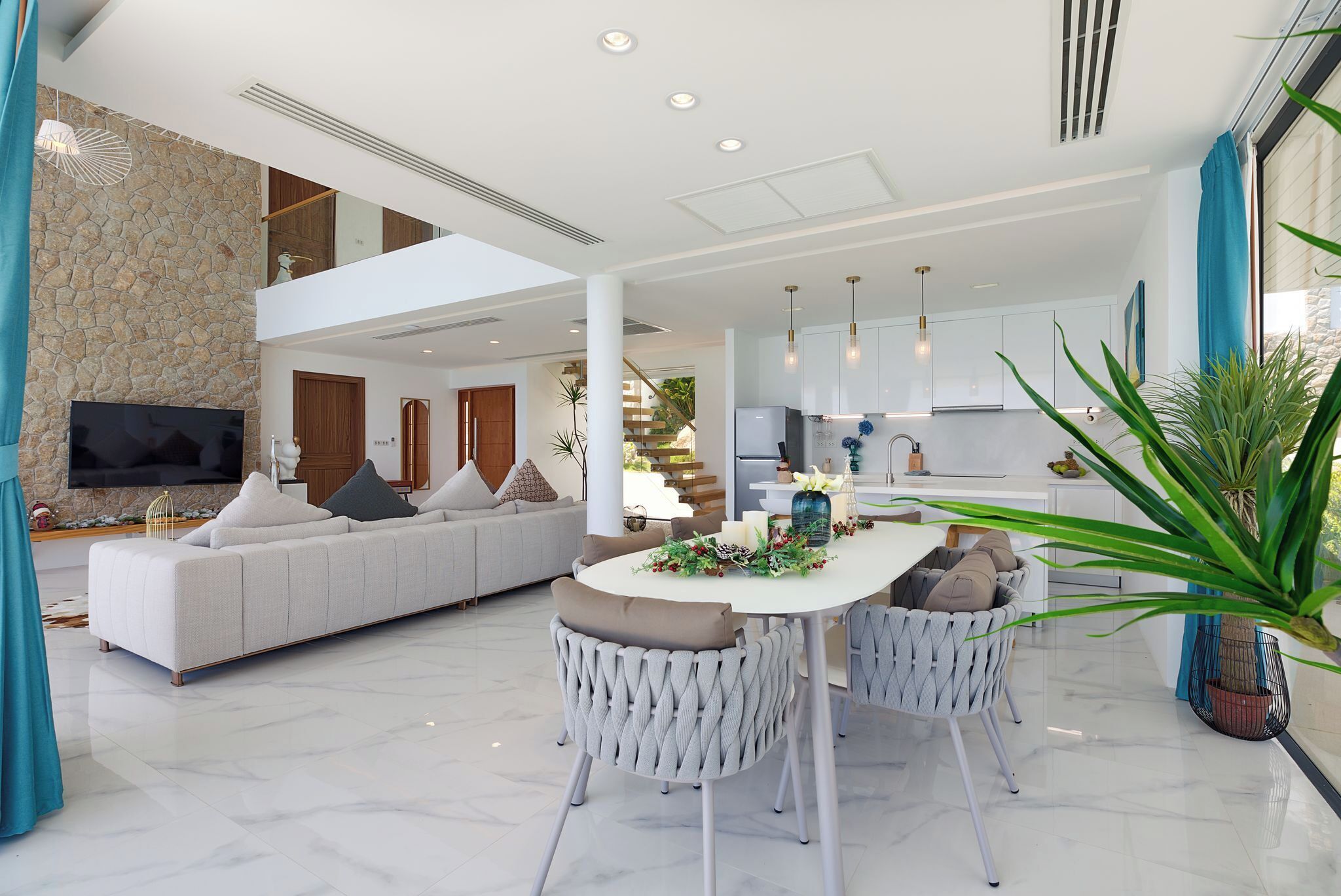 Un salon moderne avec un canapé blanc, une table à manger avec des chaises et un coin cuisine doté de meubles blancs et d’une grande fenêtre.