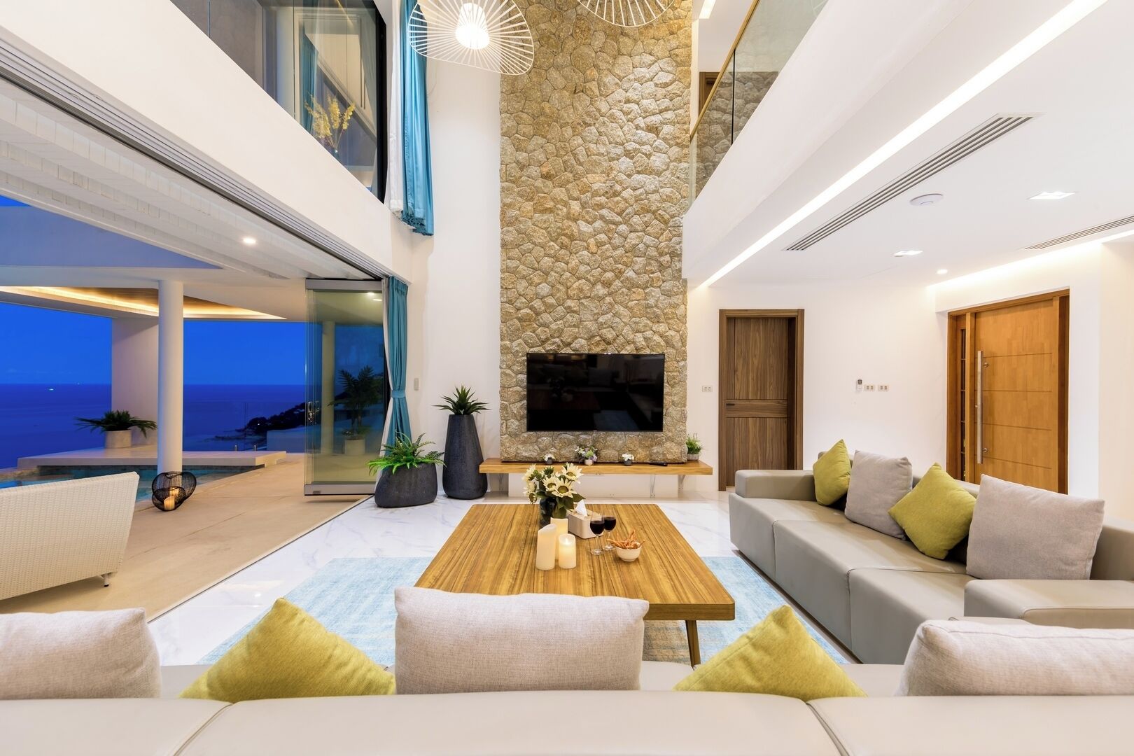 A modern living room with a stone accent wall, a flat-screen TV, and a view of the ocean.