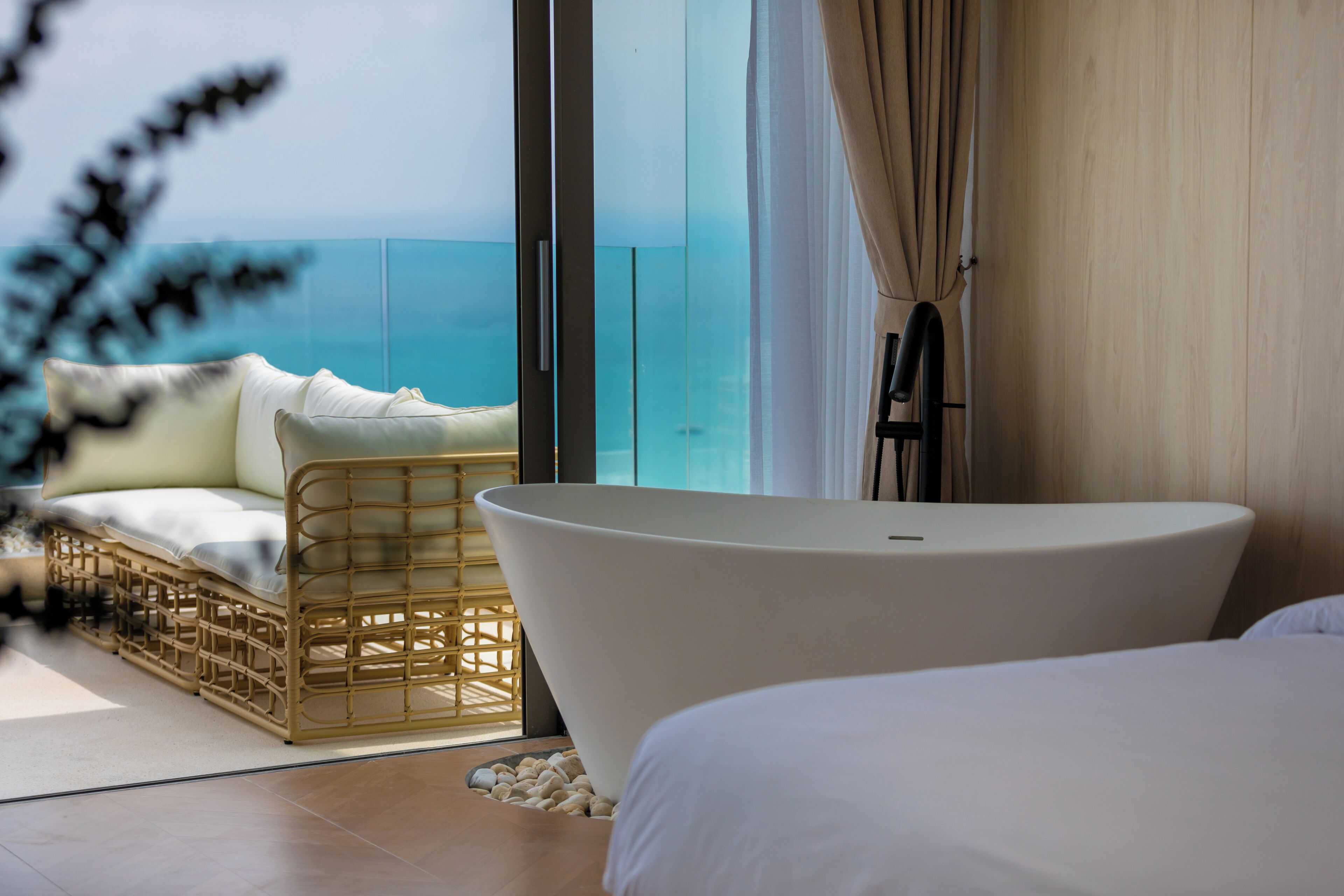Un dormitorio moderno con una bañera grande, un sofá de mimbre y vistas al mar.