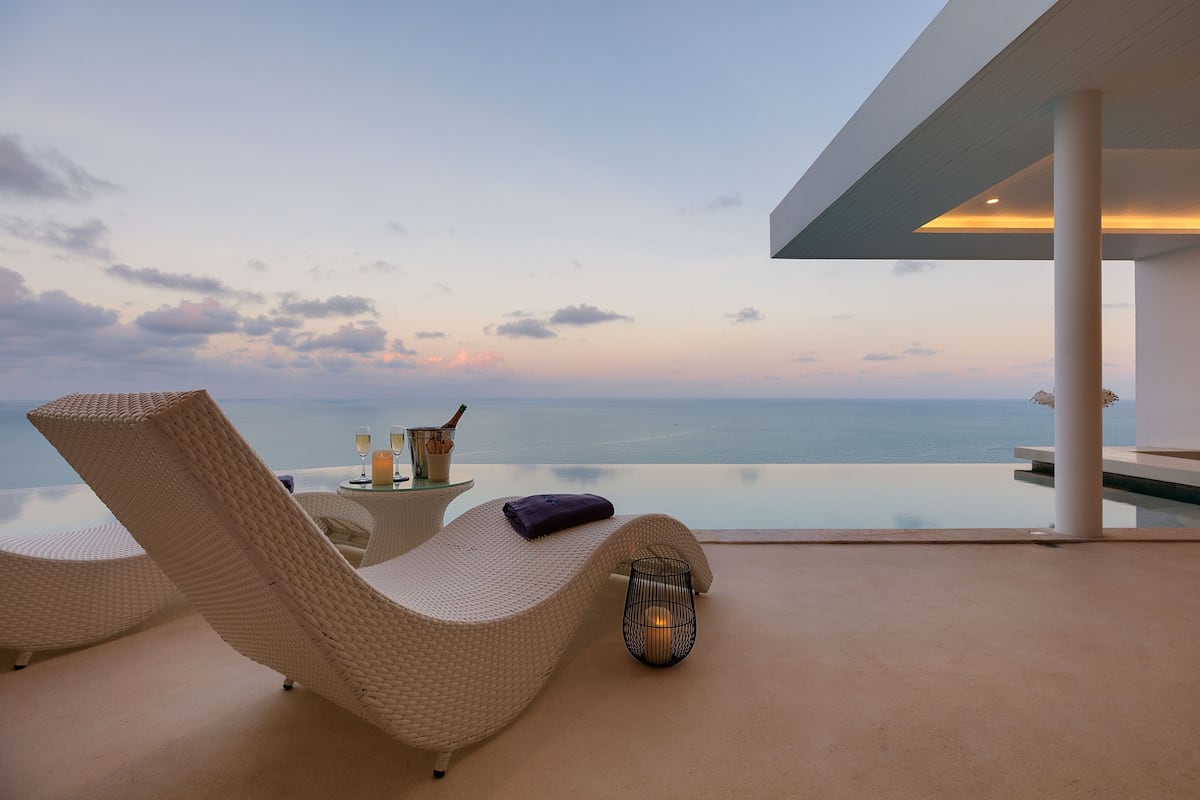 A modern lounge area with wicker chairs, a glass table with a candle, and a view of the ocean.