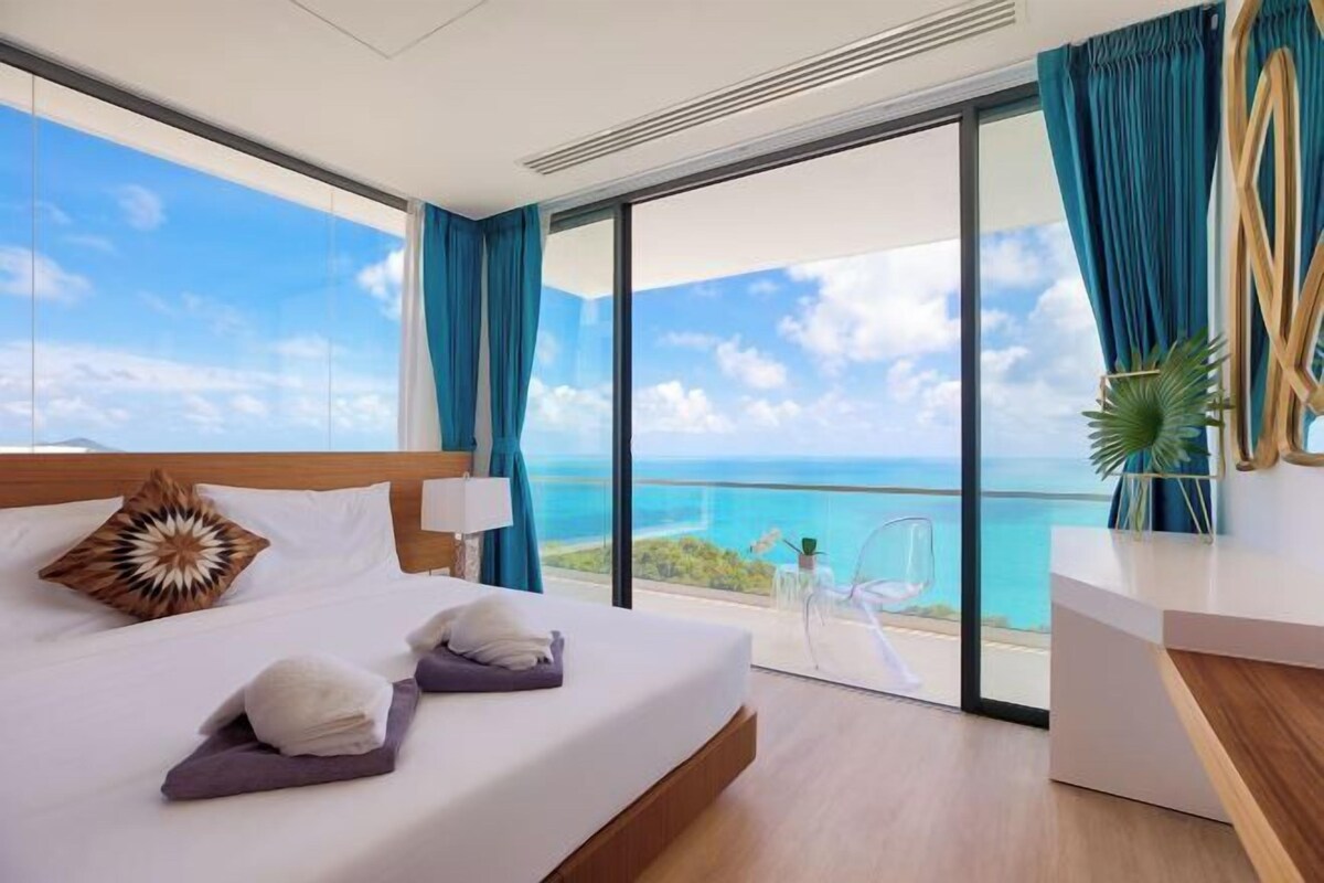 A hotel room with a large bed, a desk, a chair, and a view of the ocean.
