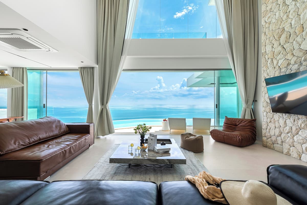 A modern living room with a large window overlooking the sea, a leather sofa, a coffee table, and a stone accent wall.