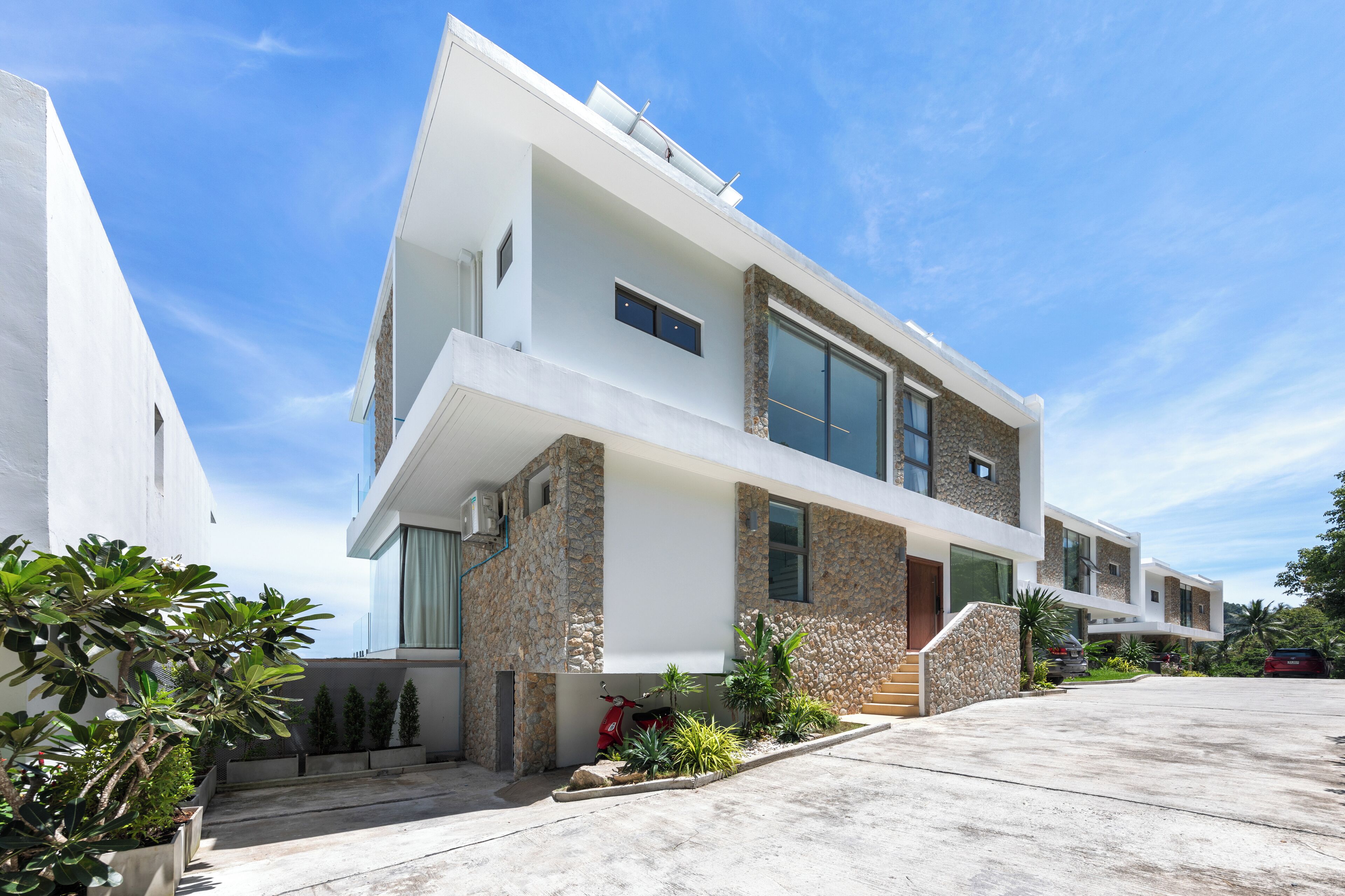 A modern two-story house with a stone facade, large windows, and a driveway.