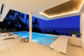 A modern outdoor pool area with lounge chairs and a view of the ocean at dusk. - Villa The Wave 2 Residence (Koh Samui)