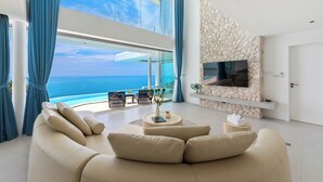 A modern living room with a large sofa, a flat-screen TV, and a stone accent wall. - Villa The Wave 2 Residence (Koh Samui)
