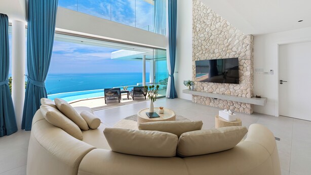 A modern living room with a large sofa, a flat-screen TV, and a stone accent wall. - Villa The Wave 2 Residence (Koh Samui)