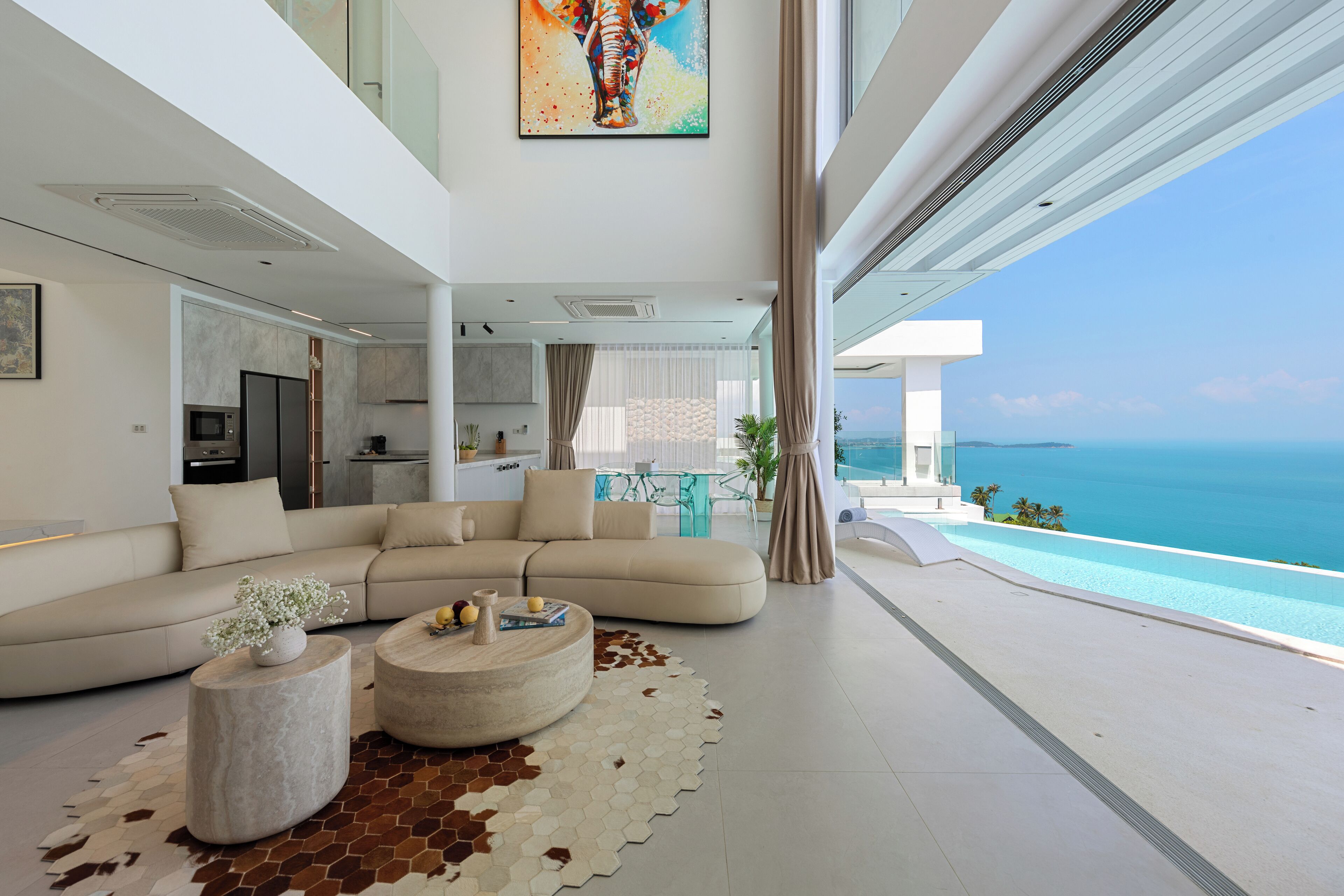 A modern living room with a large sofa, two round coffee tables, and a view of the ocean.