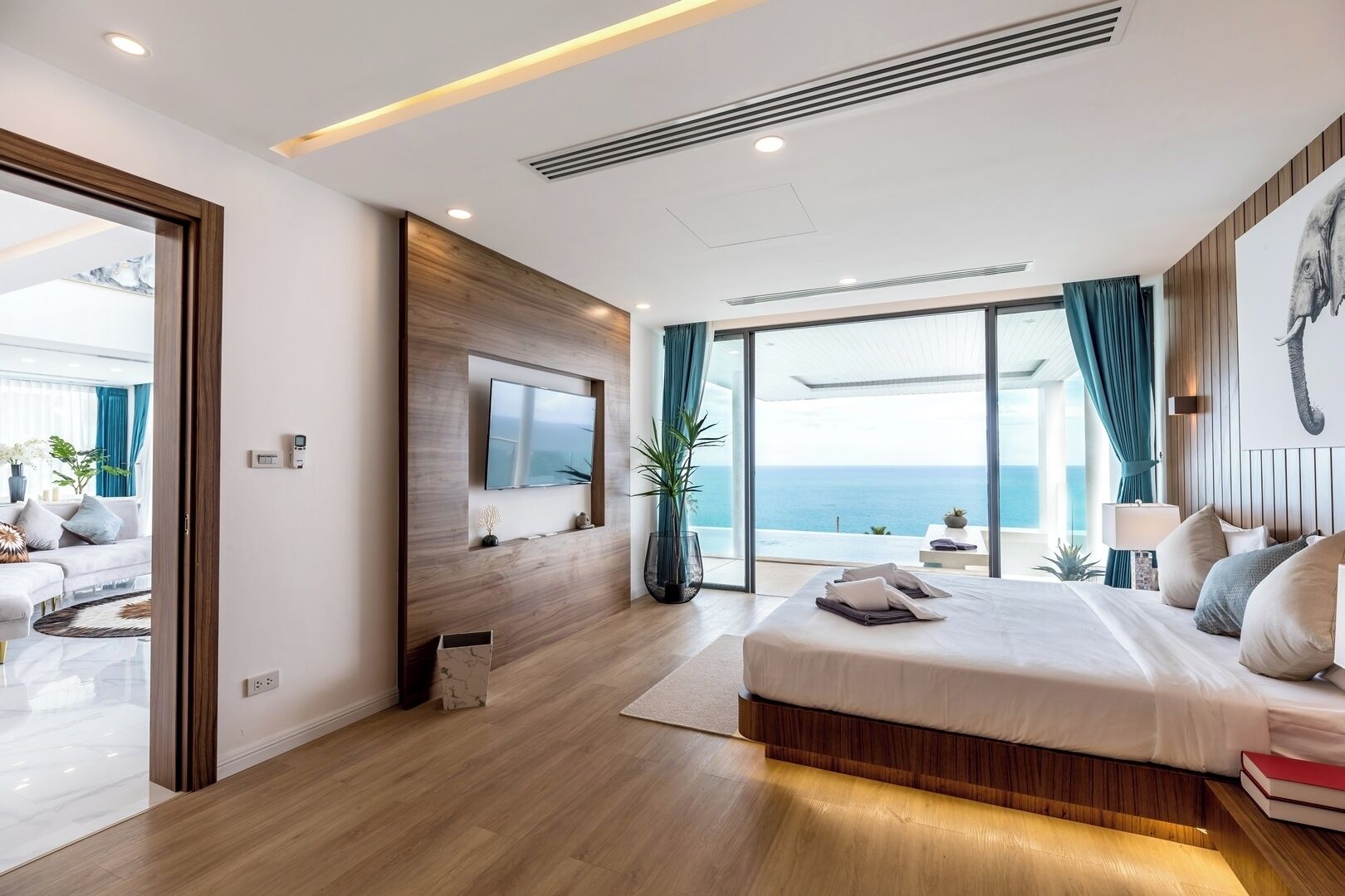 A modern bedroom with a large bed, a TV mounted on a wooden panel, a view of the sea, and a balcony with a view.