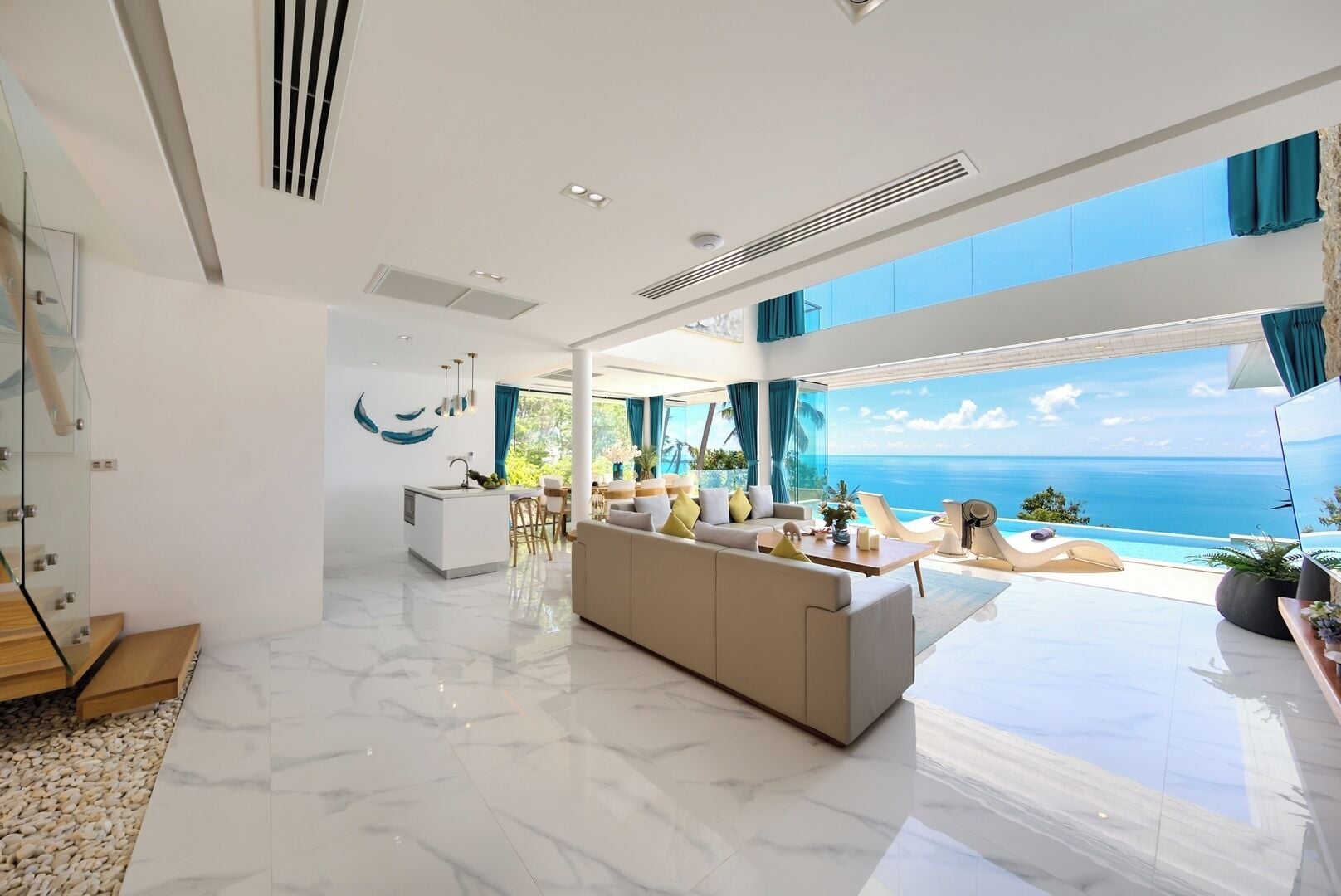 A modern living room with a large sofa, a dining area, and a view of the ocean.