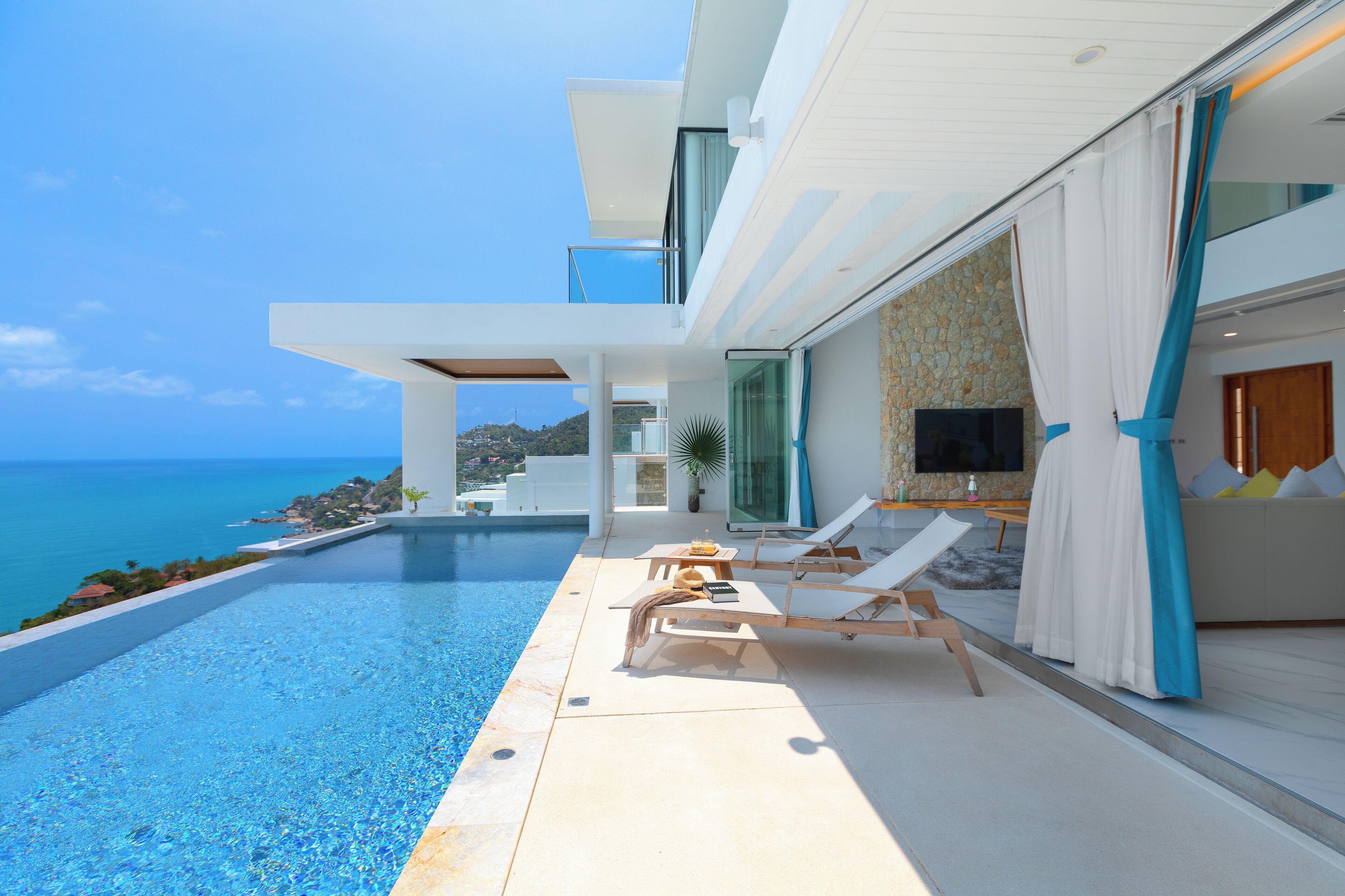 A modern house with a pool overlooking the sea, a TV in the living area, and a dining table with chairs.