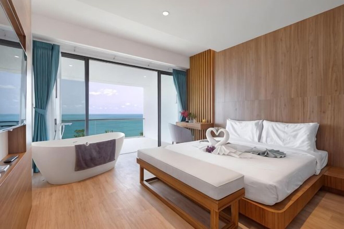 A modern hotel room with a large bed, a bathtub, and a view of the ocean.