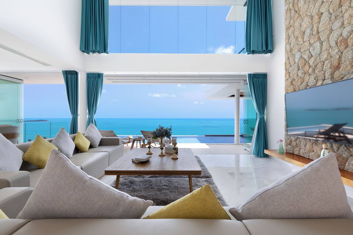 A modern living room with a view of the ocean, a stone wall, and a flat-screen TV.