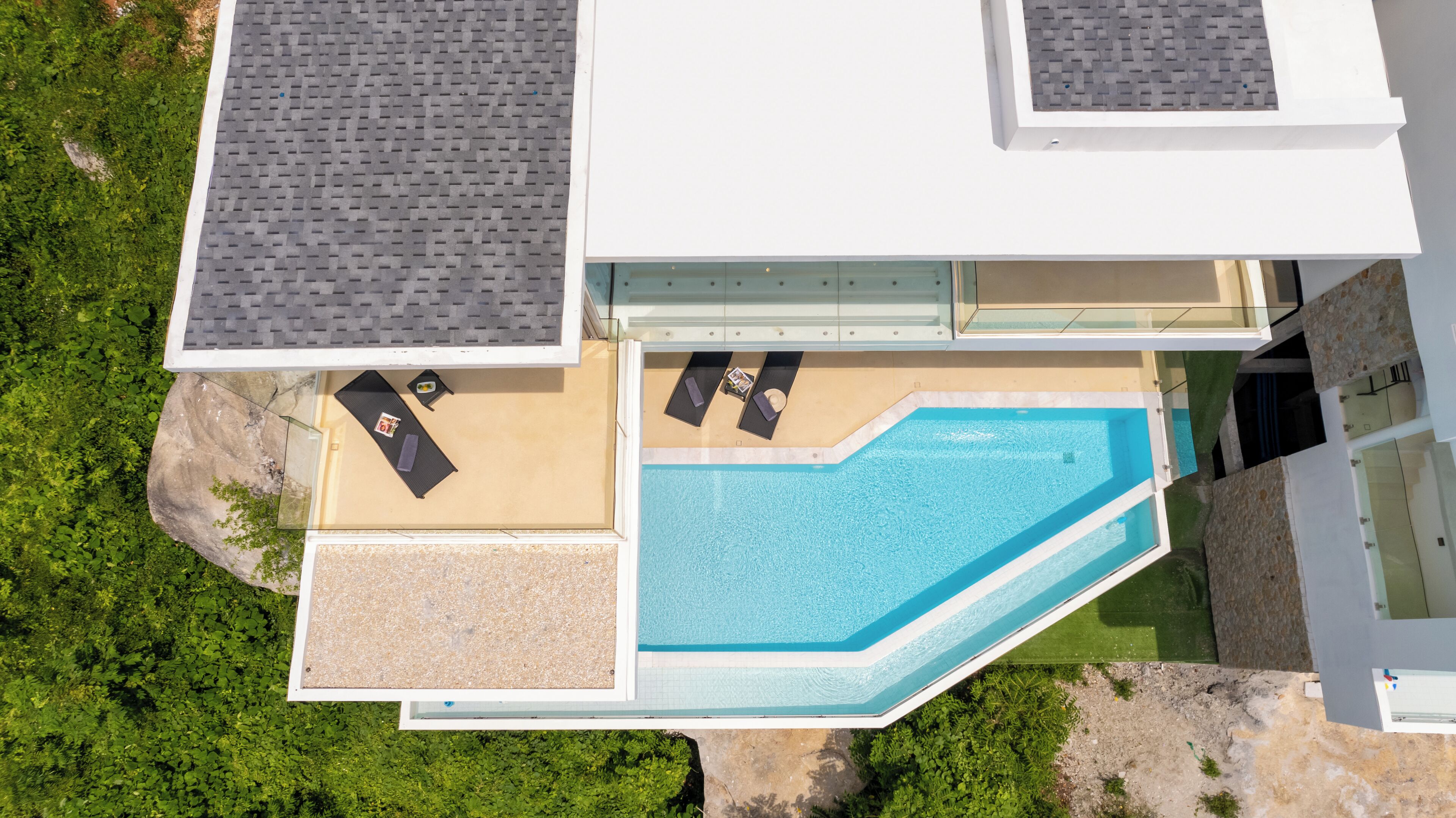 An aerial view of a modern building with a swimming pool, two lounge areas with sun loungers, and a small deck area.