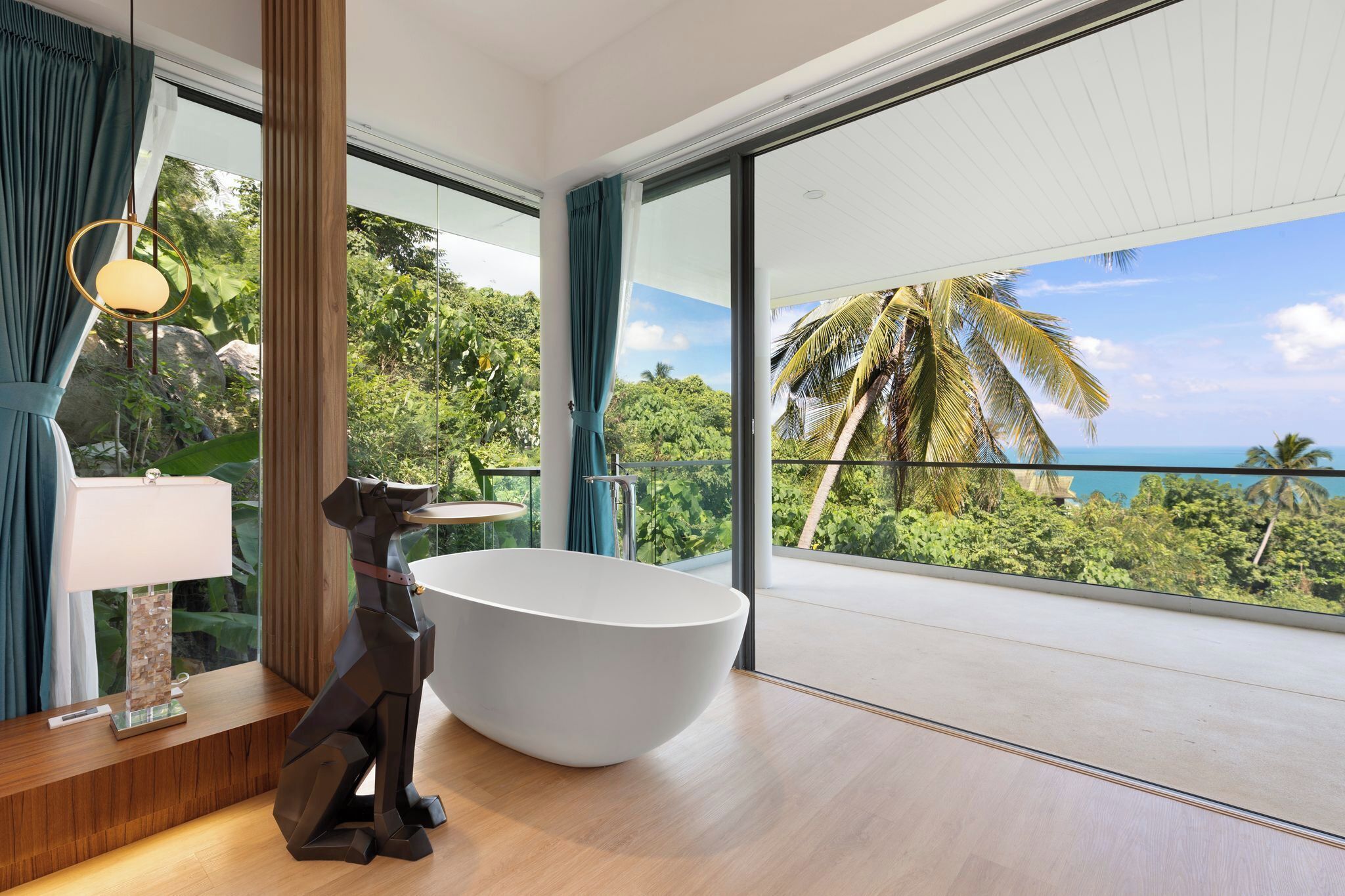 A modern bathroom with a freestanding bathtub, large windows, and a view of a tropical landscape.