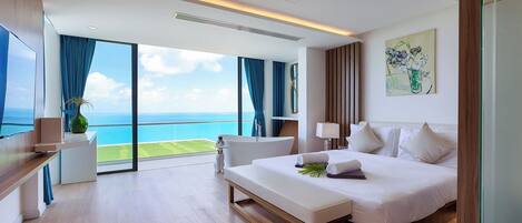 A modern hotel room with a large bed, a bench, a desk, and a view of the ocean.