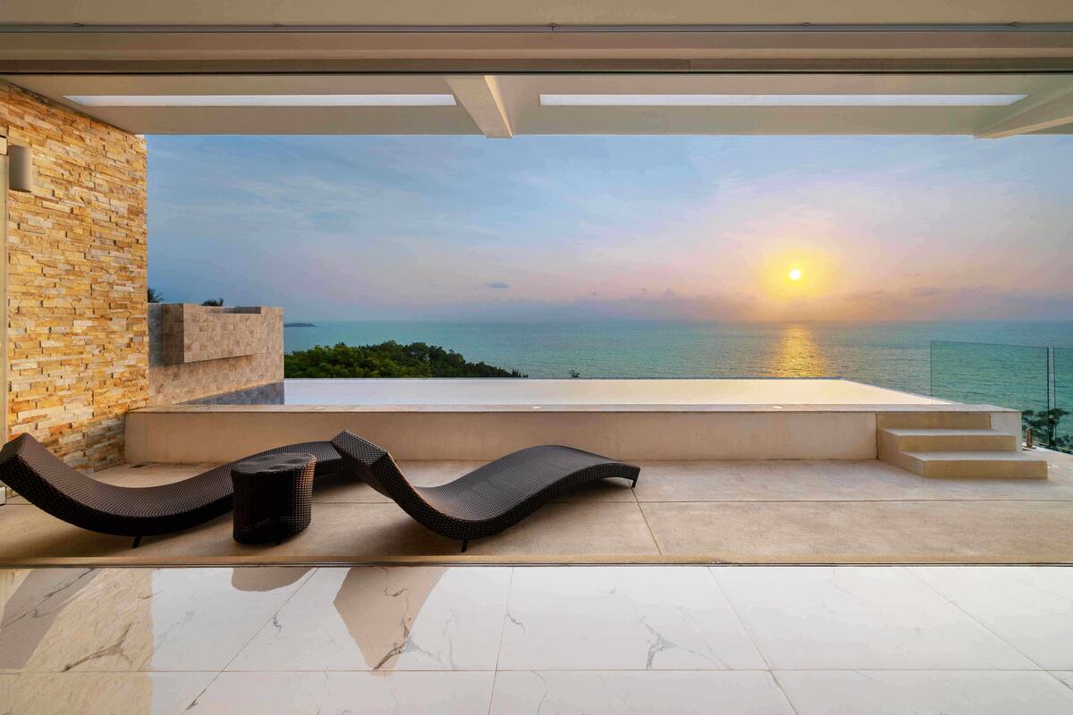 A modern outdoor seating area with a view of the sea at sunset.