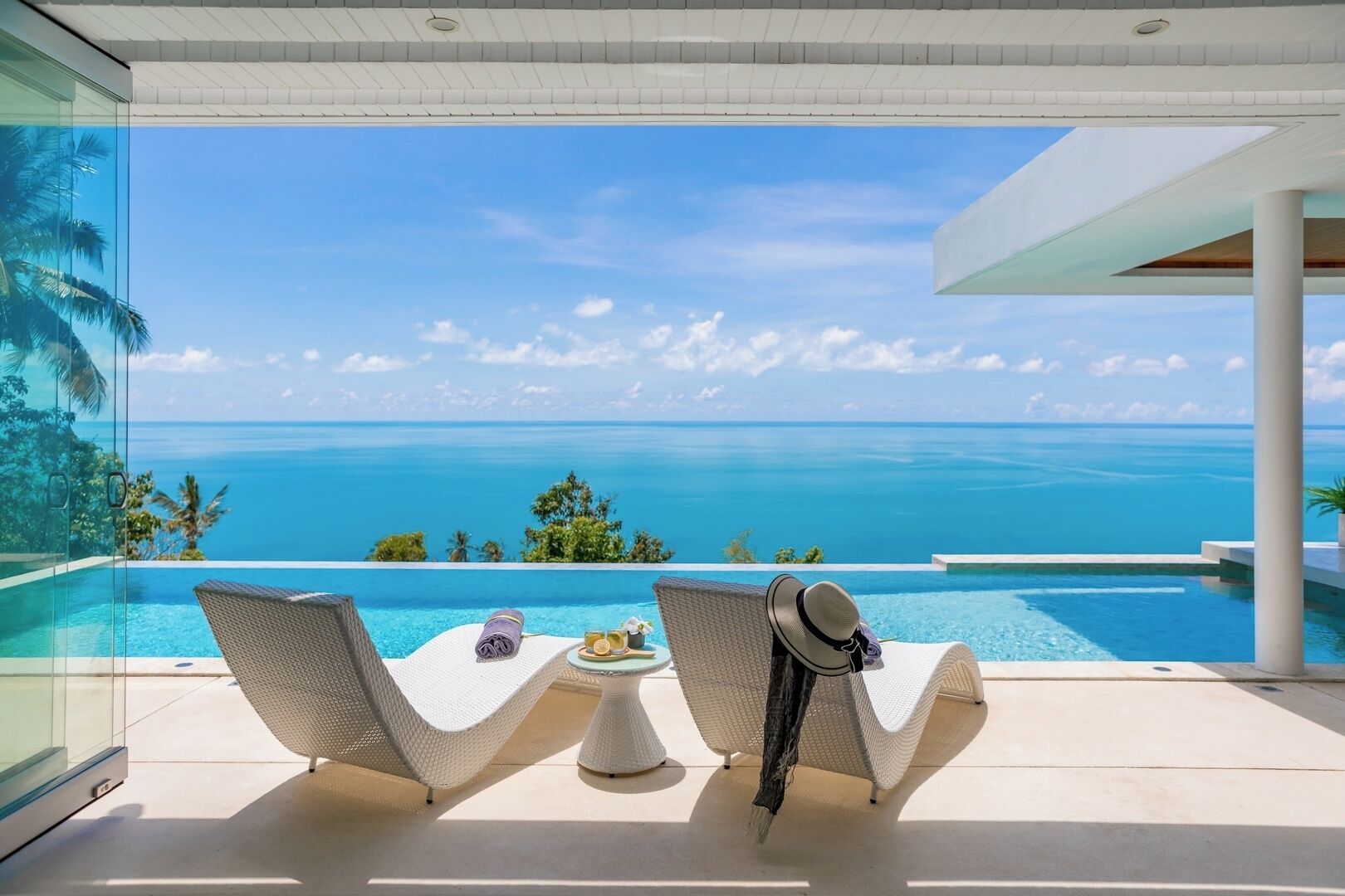 A modern outdoor seating area with two wicker lounge chairs facing a infinity pool and ocean view.
