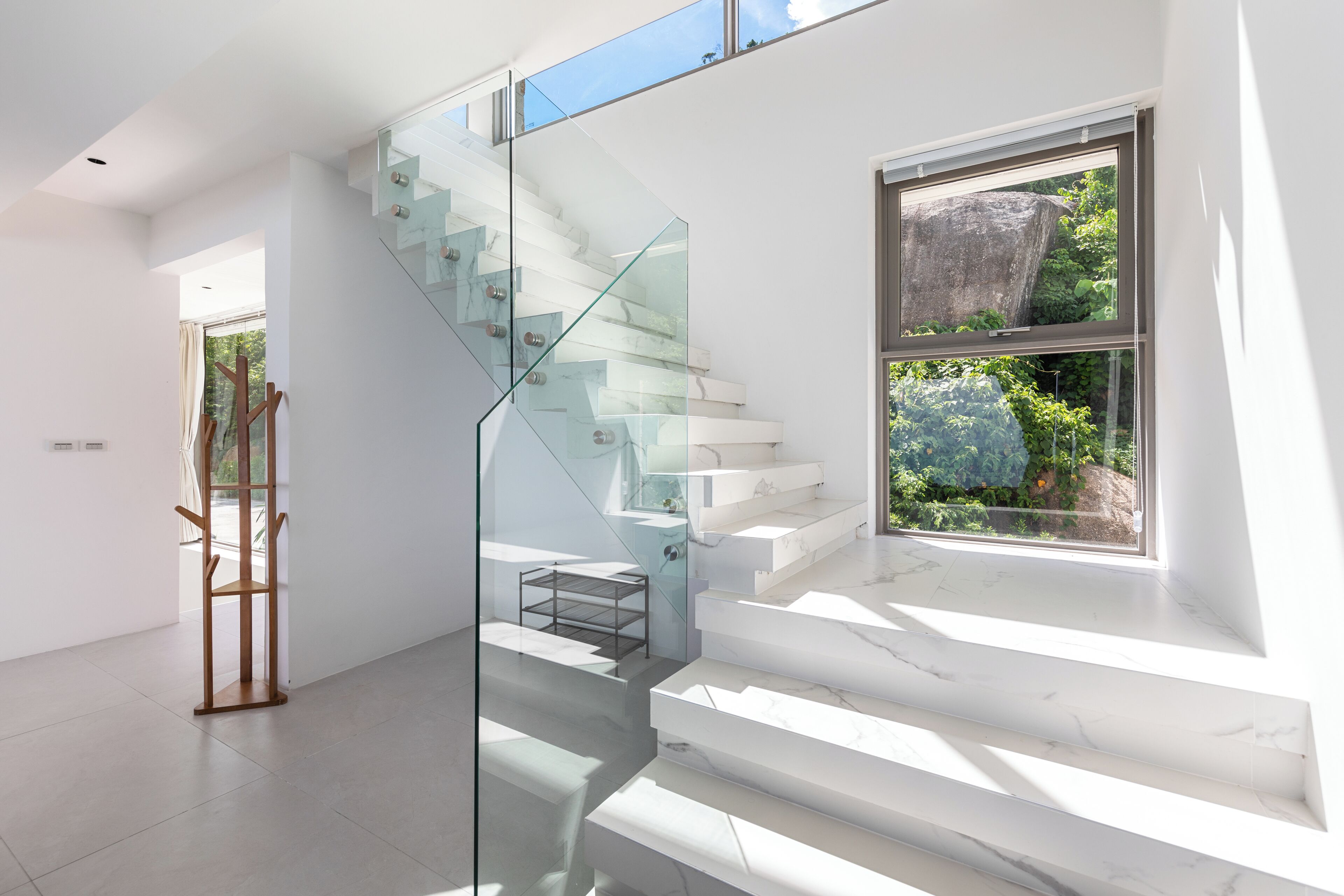 A modern staircase with glass railings, a view of greenery outside, and a minimalist interior design.