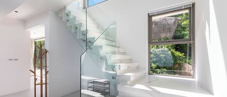 A modern staircase with glass railings, a view of greenery outside, and a minimalist interior design.