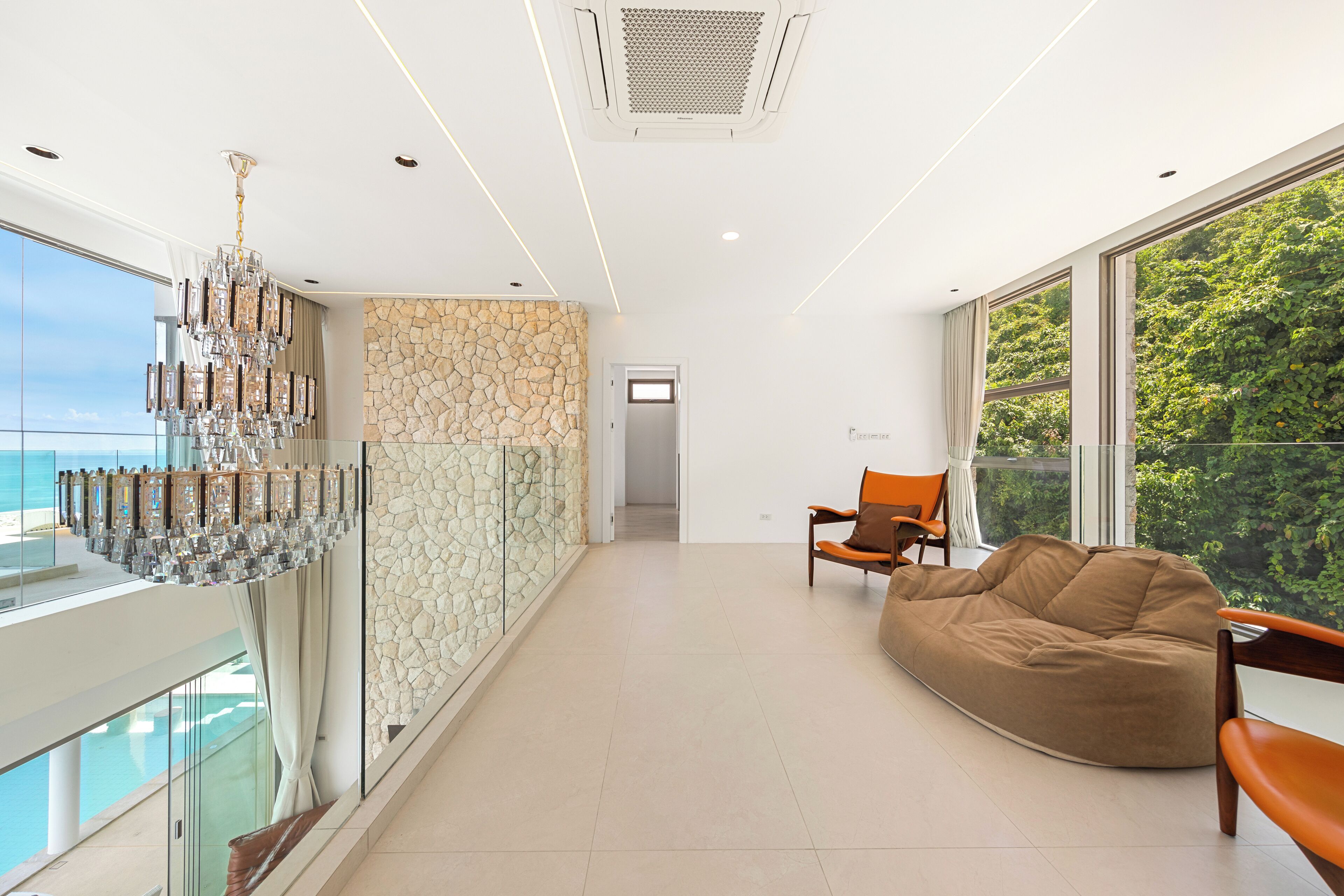 Een modern interieur met een groot raam, een stenen muur, een kroonluchter en een relax fauteuil.