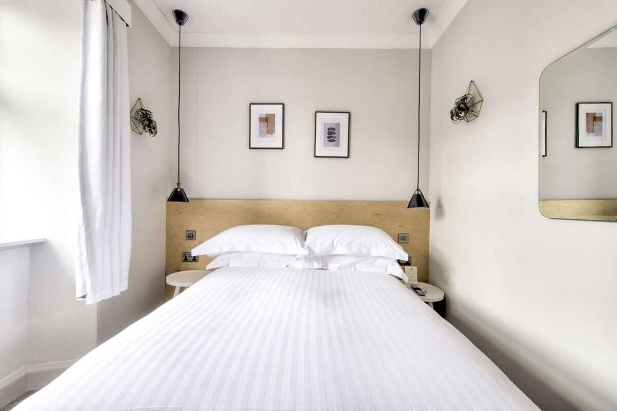 A hotel room with a large bed, bedside tables, a mirror, and framed pictures on the wall.