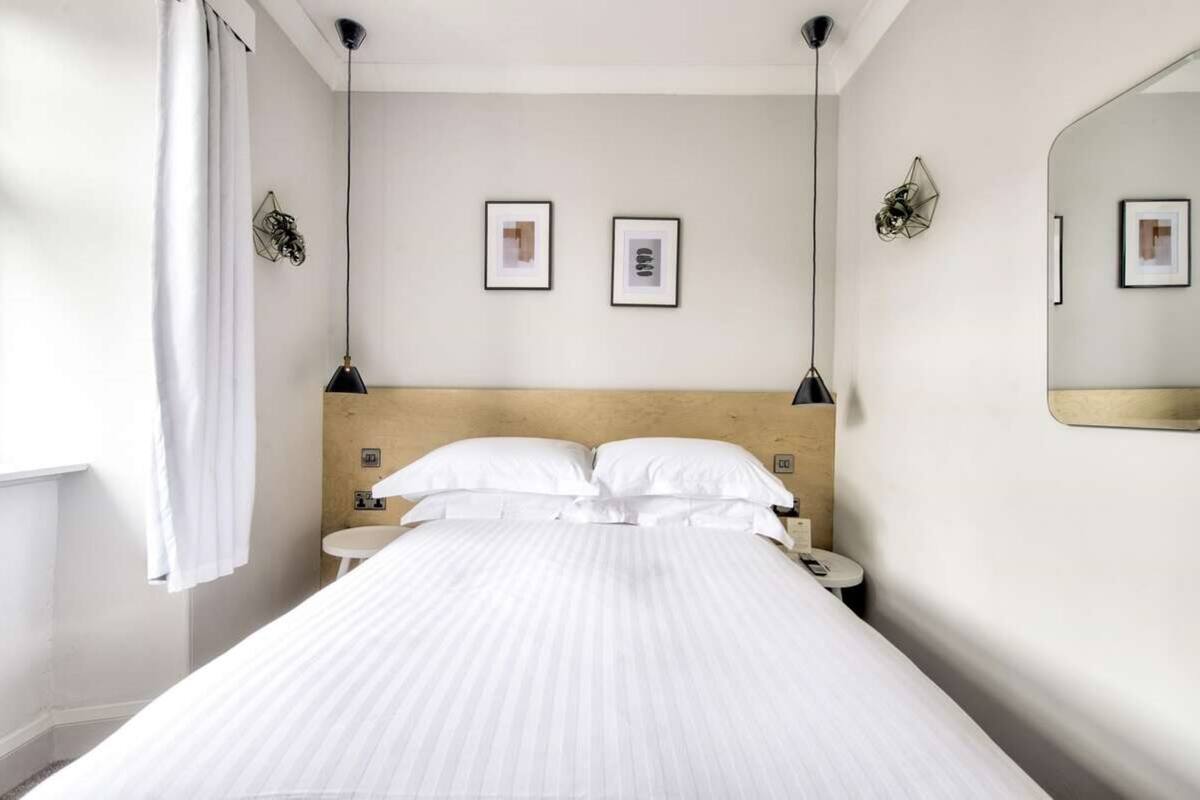 A hotel room with a bed, two bedside tables, a wall-mounted mirror, and two framed pictures on the wall.