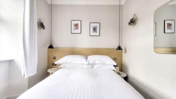 A hotel room with a bed, two bedside tables, a wall-mounted mirror, and two framed pictures on the wall.