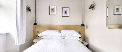 Habitación de hotel con una cama, dos mesitas de noche, un espejo montado en la pared y dos cuadros enmarcados.