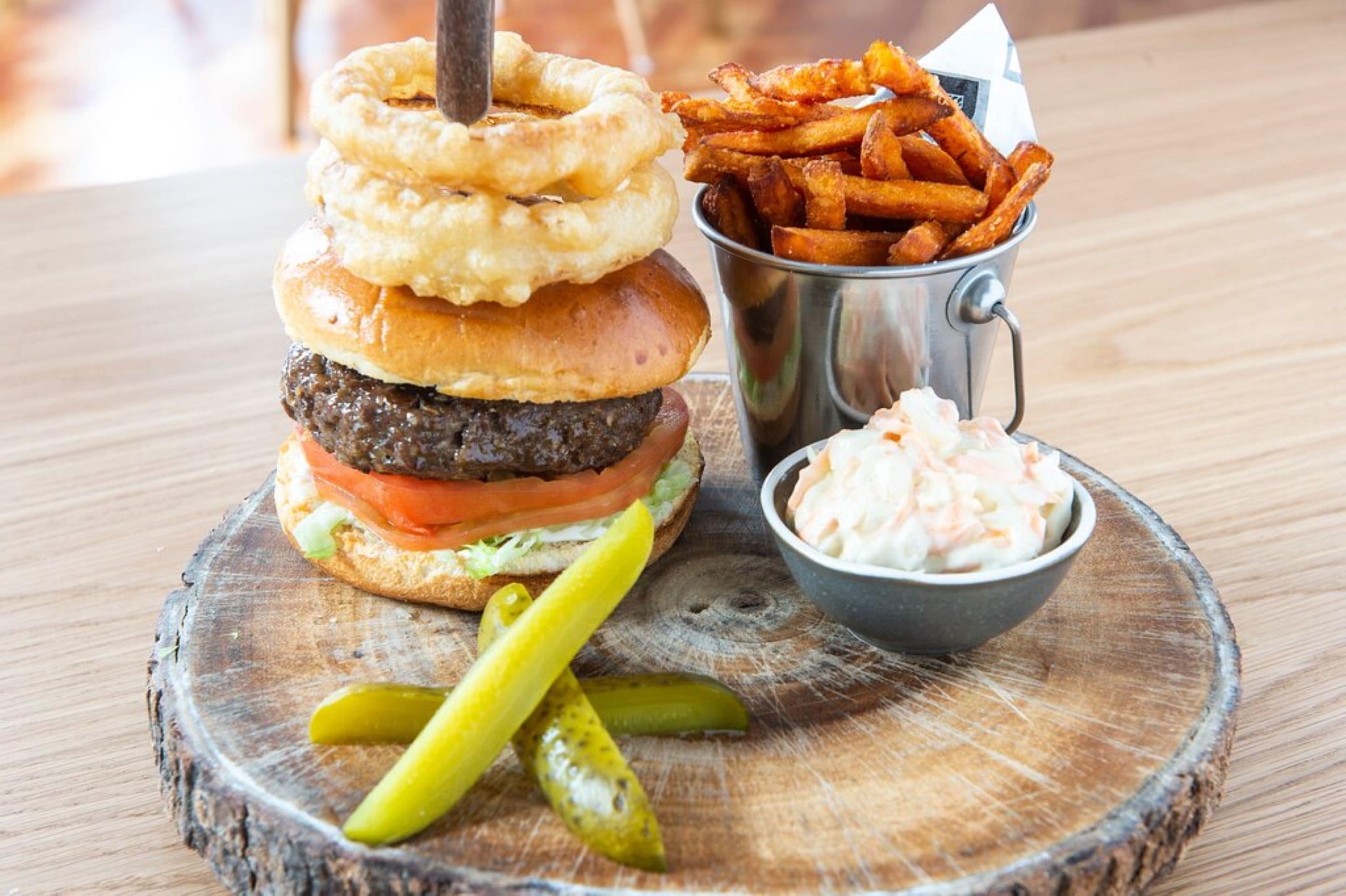 A burger with onion rings, fries, and coleslaw on a wooden board.