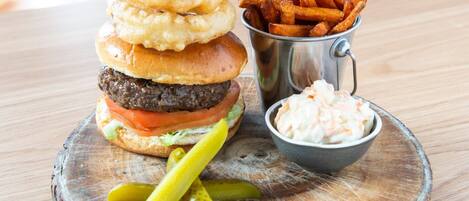 Ein Burger mit Zwiebelringen, Pommes und Krautsalat auf einer Holzbrett.