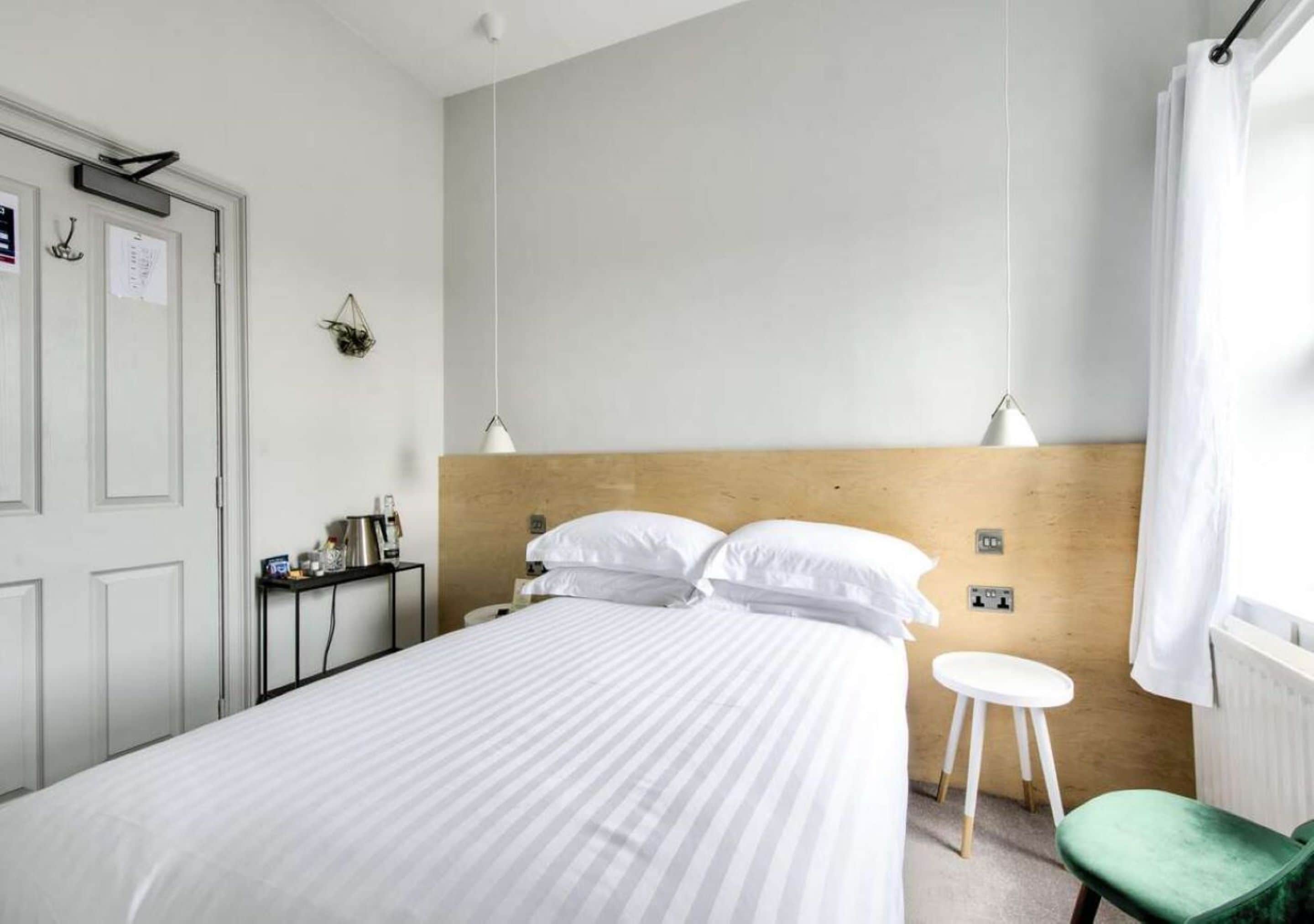 A hotel room with a bed, bedside table, lamp, and a small stool.