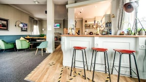 A modern bar area with a white countertop, three red bar stools, and a visible bar stocked with bottles. - The Castle Hotel (Berwick-upon-Tweed)