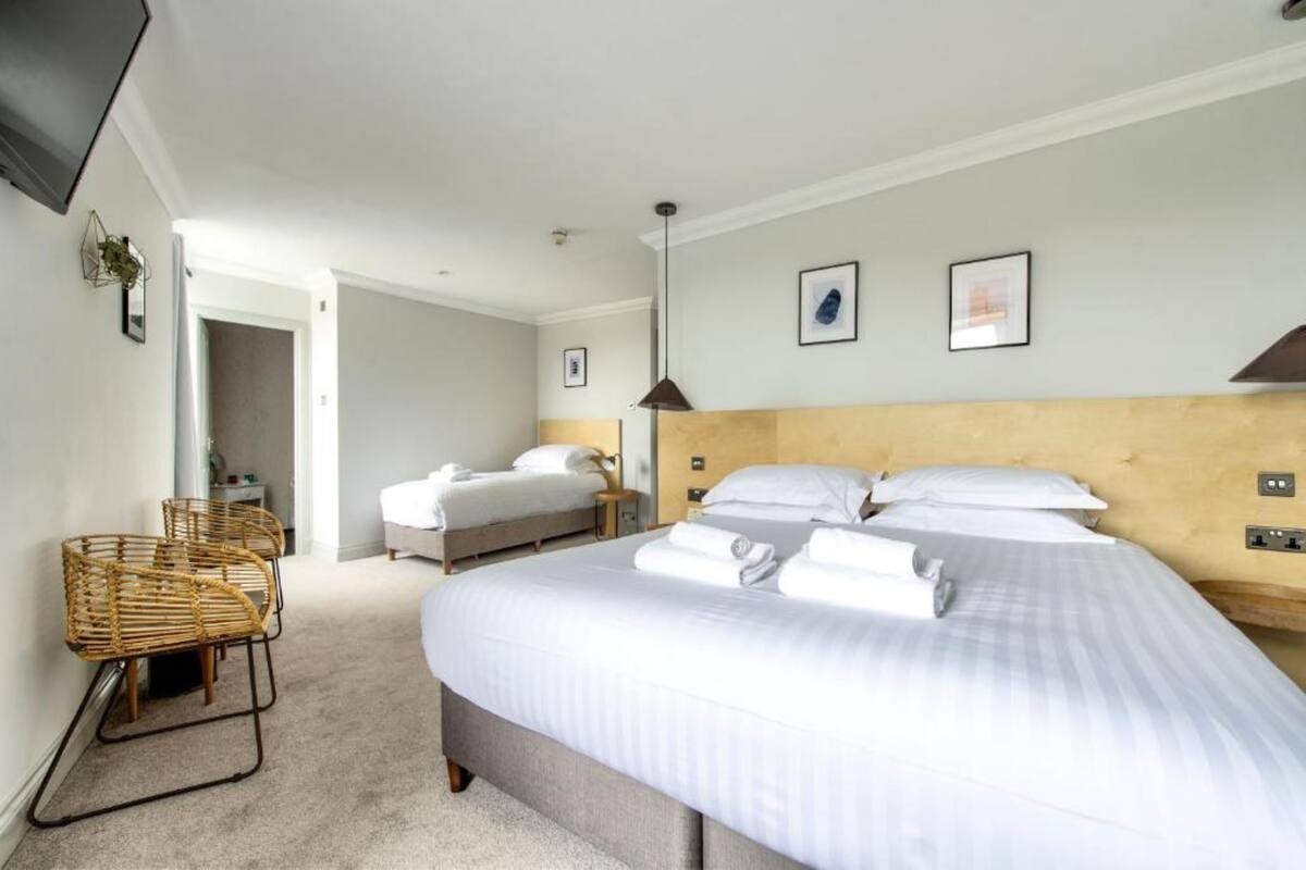 A hotel room with two beds, a large window, a wooden headboard, and a wicker chair.