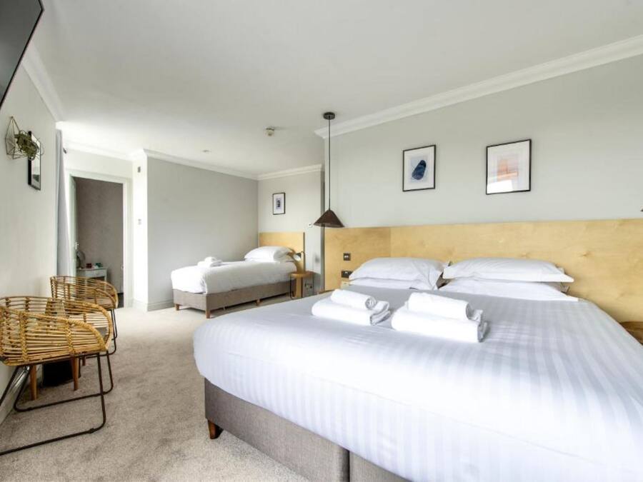 Habitación de hotel con dos camas, un ventanal grande, cabecera de madera y una silla de mimbre.