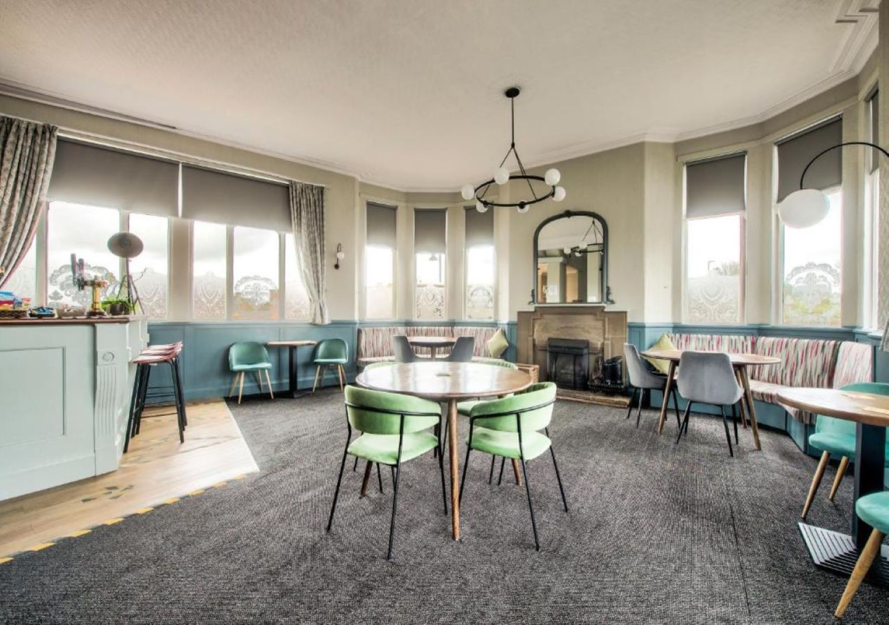 Een gezellige eethoek met een ronde tafel en stoelen, een open haard en grote ramen voorzien van gordijnen.