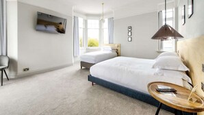 A hotel room with two beds, a TV mounted on the wall, a desk with a lamp, and a view of the outdoors through the window. - The Castle Hotel (Berwick-upon-Tweed)