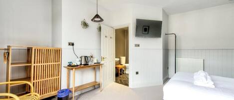 Une chambre d’hôtel avec un lit, une étagère en bois, une table avec une lampe et un téléviseur fixé au mur.