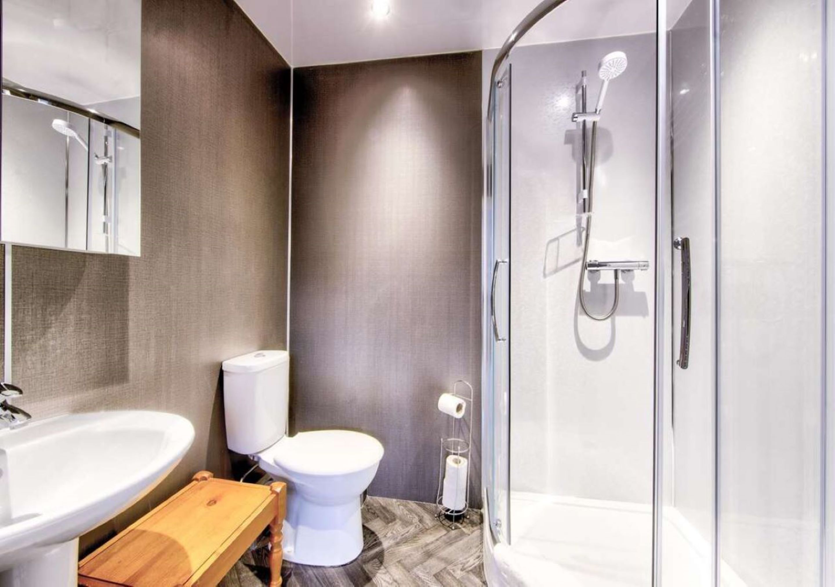 A modern bathroom with a glass-enclosed shower, a white toilet, and a wooden vanity with a sink.