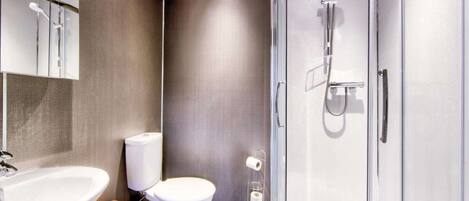 Een moderne badkamer met een douche met glazen wand, een wit toilet en een houten wastafelmeubel met een wastafel.