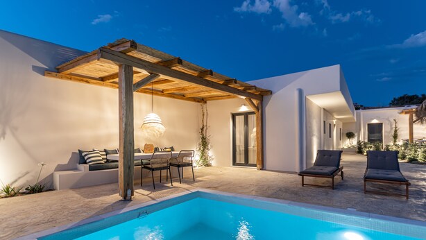 A modern outdoor pool area with a pergola, lounge chairs, and a dining setup. - Golden Sand Villas (Naxos)