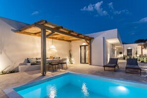 A modern outdoor pool area with a pergola, lounge chairs, and a dining setup. - Golden Sand Villas (Naxos)