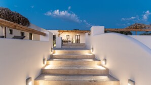 A staircase leading to a building with a thatched roof, illuminated by wall-mounted lights. - Golden Sand Villas (Naxos)