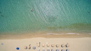 An aerial view of a beach with rows of beach umbrellas and chairs, a clear blue sea, and a sandy shore. - Golden Sand Villas (Naxos)