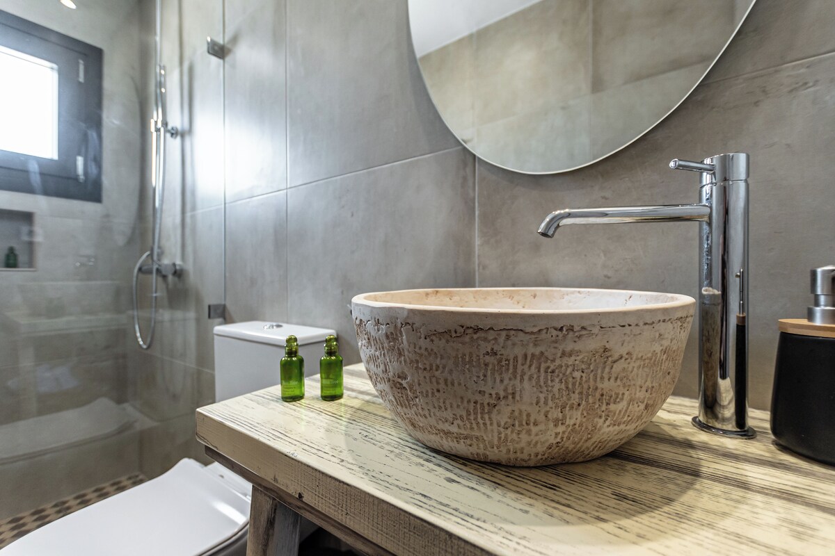 A bathroom with a large ceramic sink, a modern faucet, and a glass shower enclosure.