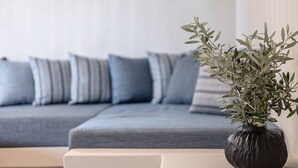 A modern living room with a grey sofa, striped cushions, and a dark vase with green foliage. - Golden Sand Villas (Naxos)