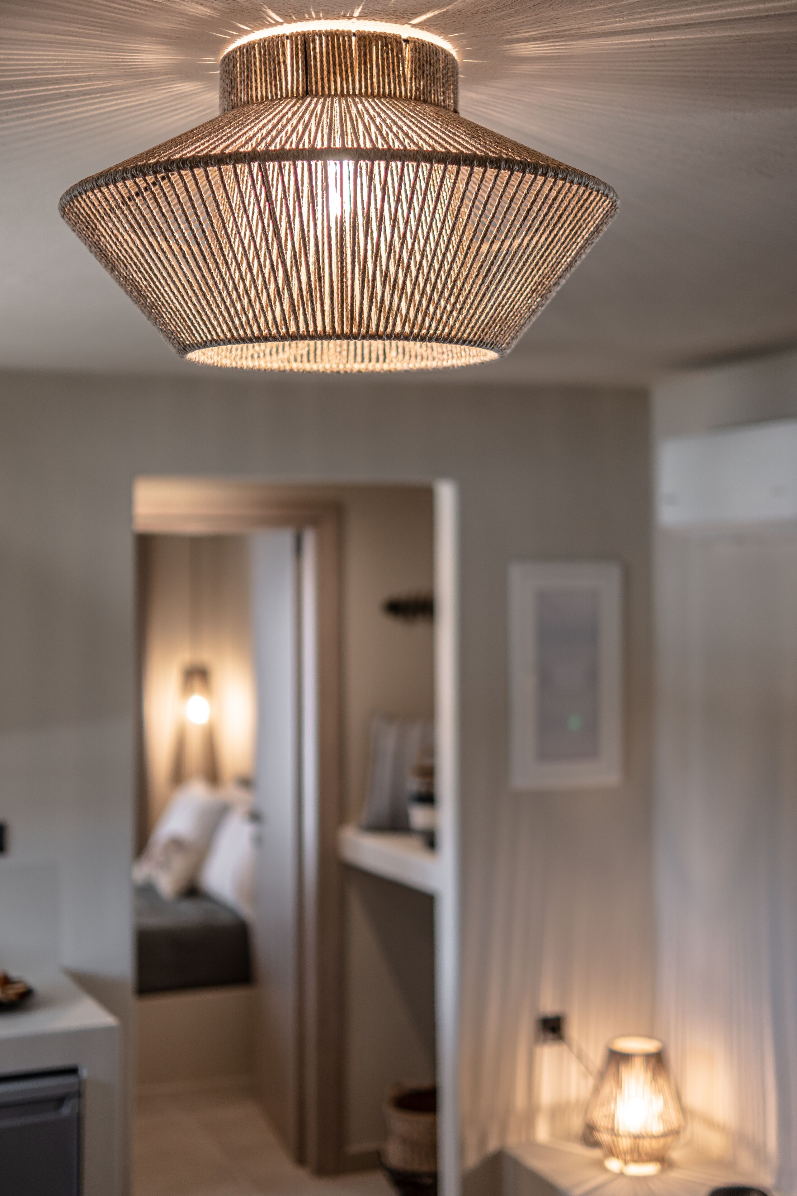 Un intérieur moderne avec un luminaire au plafond à texture intéressante et un arrière-plan flou évoquant une pièce chaleureuse avec un lit et un bureau.